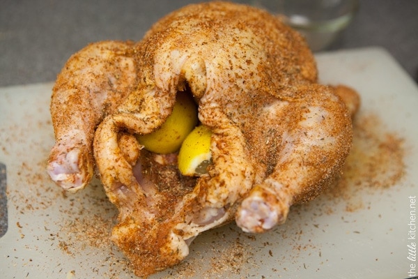 whole chicken on a cutting board with spice rub and stuffed with lemon