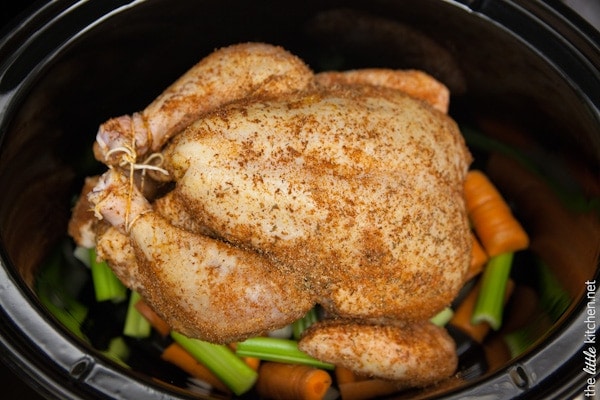 hela kycklingen med kryddor placerad ovanpå grönsaker i en slow cooker