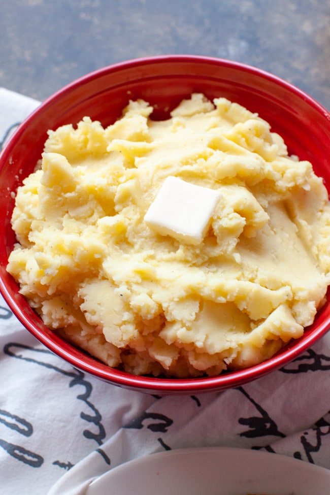 A large red bowl with mashed potatoes and butter on top