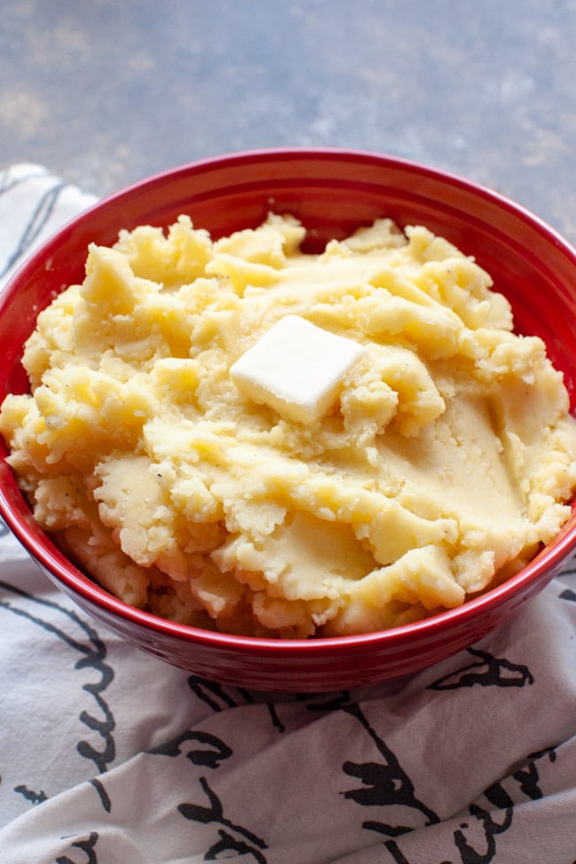 A large red bowl with mashed potatoes and butter on top