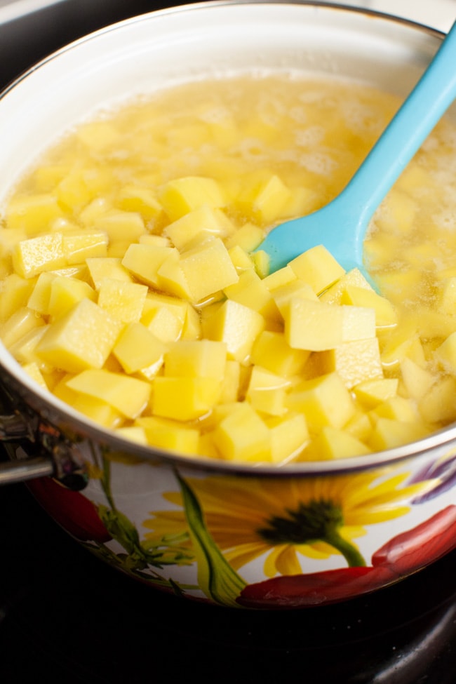 cut up potatoes in a pot of water with a blue rubber spatula