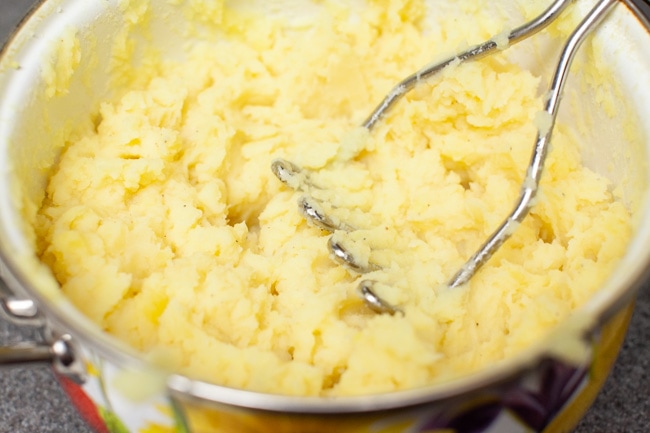 mashed potatoes in a pot with potato masher