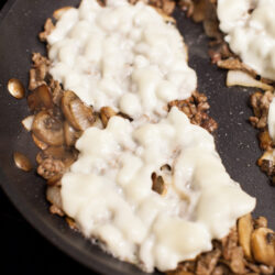 meat and cheese cooking in a nonstick skillet for cheesesteaks