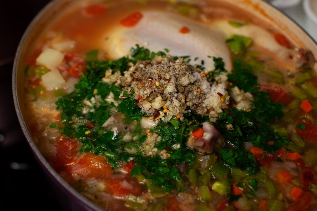 whole chicken in a soup pot with chopped parsley and other herbs on top