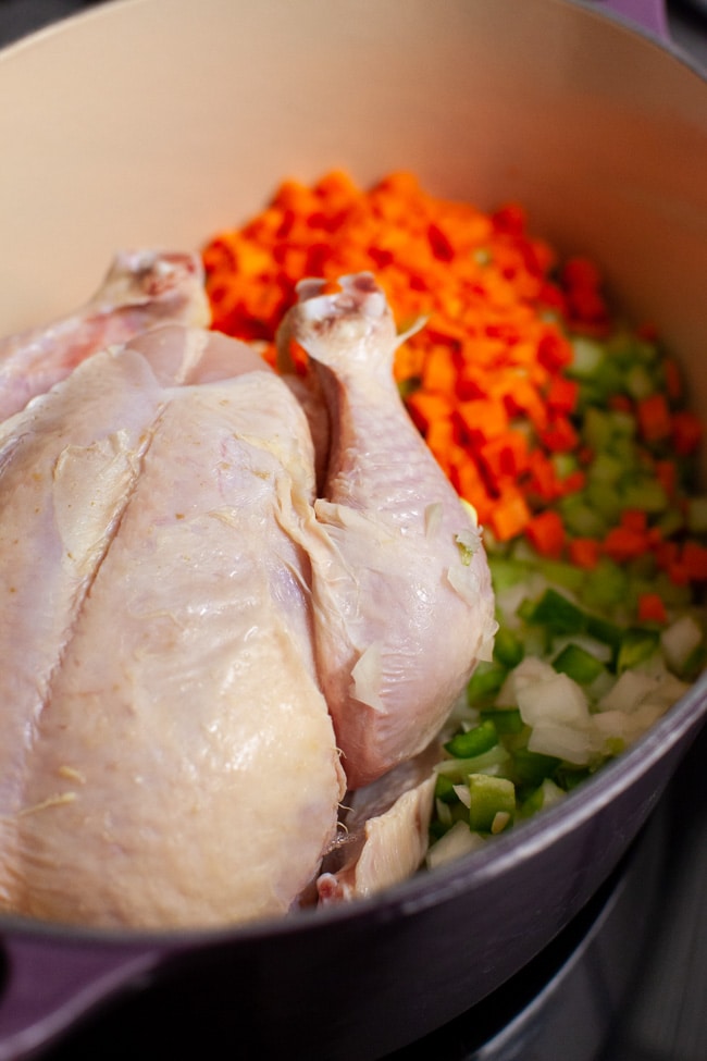 a whole chicken in a pot with chopped carrots, celery and onions