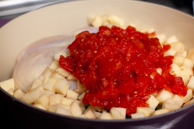 a pot with a whole chicken, chopped potatoes and diced canned tomatoes on top