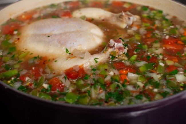 a whole chicken in a pot cooking with vegetables, parsley and spices