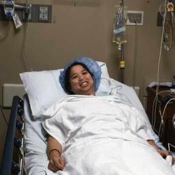 a woman laying in a hospital bed with a hair net on with white blankets