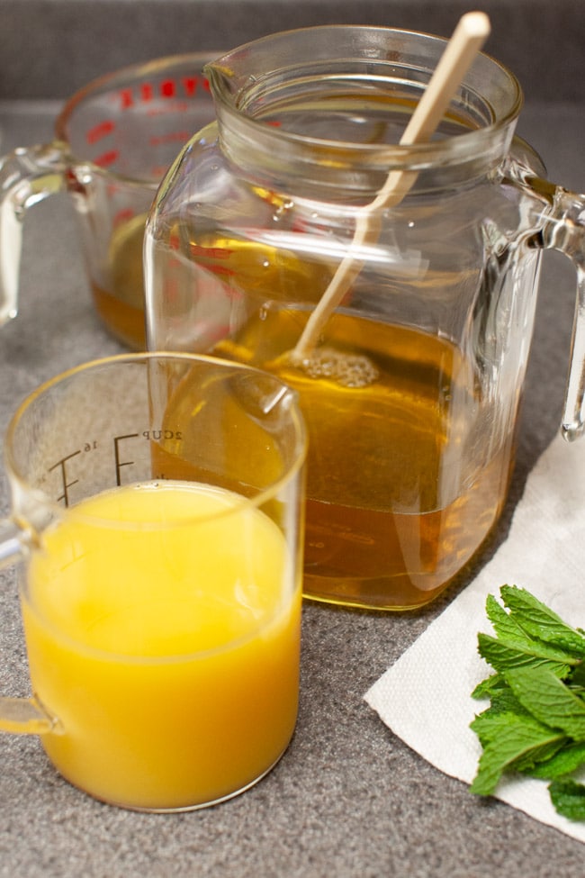 orange juice in a cup with tea in a glass jug and fresh mint leaves on a kitchen counter