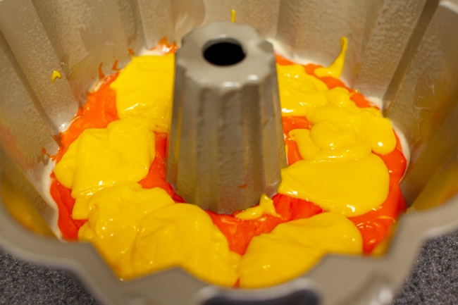 Yellow cake batter poured on top of orange cake batter in Bundt cake pan