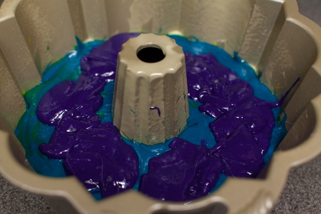 Purple cake batter being poured on top of blue cake batter in Bundt cake pan