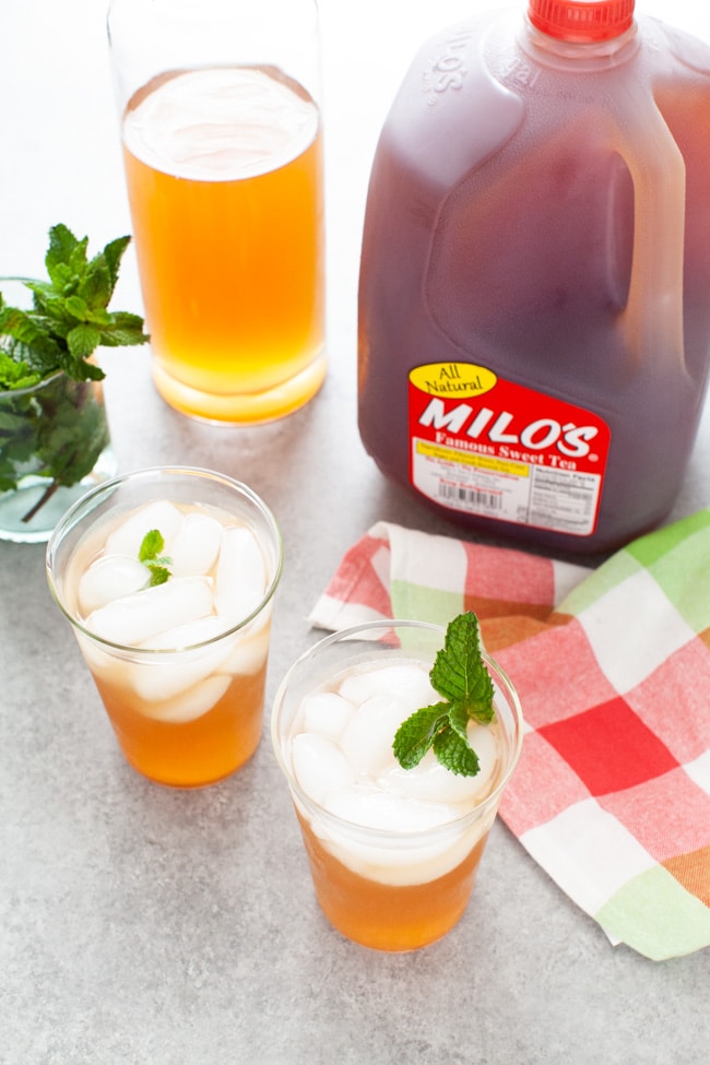 glasses with sweet tea vodka and lemonade with jug of Milo's Sweet Tea in the background, glass with fresh mint