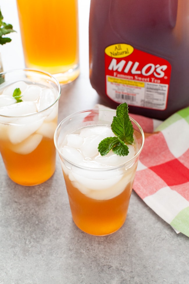 glasses with sweet tea vodka and lemonade with jug of Milo's Sweet Tea in the background