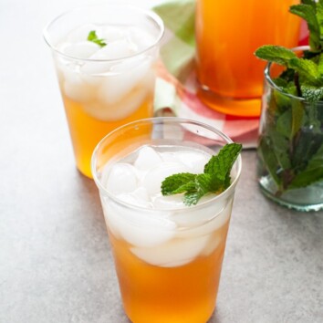 glasses with sweet tea vodka and lemonade with fresh mint in a glass on the side and a pitcher of the same drink in the background