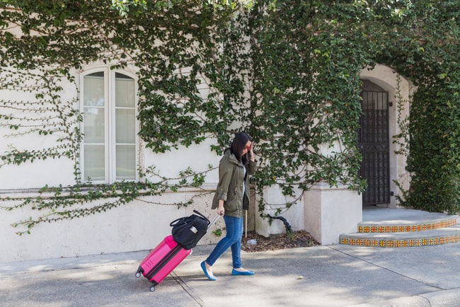 a woman rolling a suitcase and a carry on bag on the sidewalk