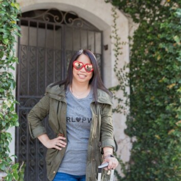 a woman standing next to a suitcase and a carry on bag on the sidewalk wearing heart-shaped sunglasses