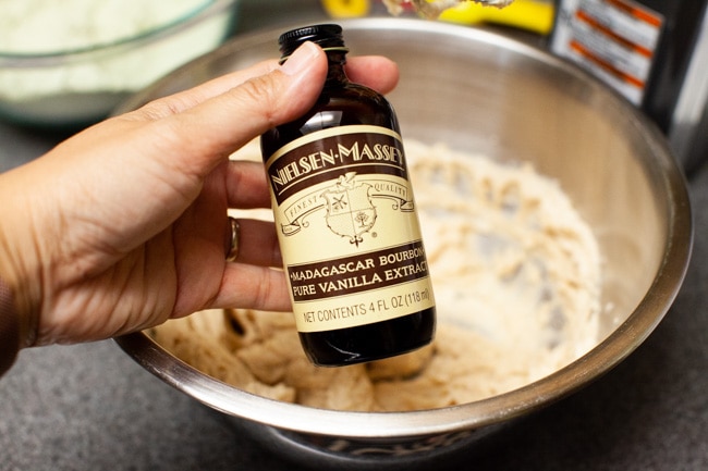 Hand holding bottle of vanilla extract with mixing bowl in background for Matcha Cookies from thelittlekitchen.net