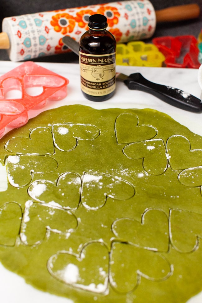 Matcha Cookie dough with heart-shaped cookie cutter impressions with bottle of vanilla, spatula, cookie cutter, and rolling pins in background from thelittlekitchen.net
