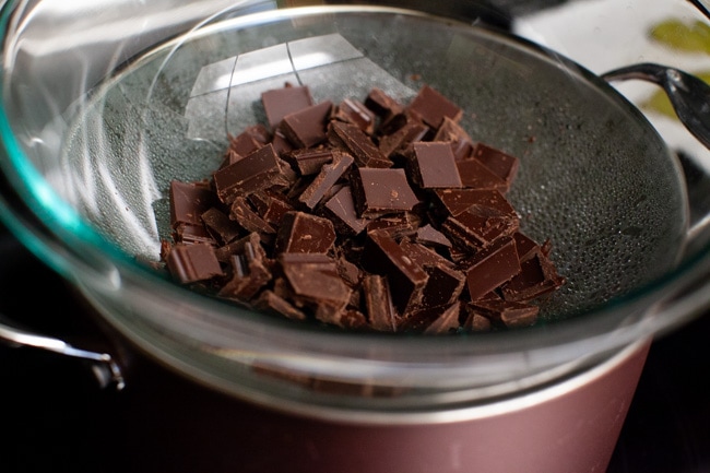 Roughly chopped chocolate pieces in a glass bowl set over simmering water in a saucepan from thelittlekitchen.net