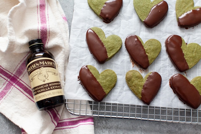 Heart Shaped Chocolate Dipped Matcha Cookies on cooling rack next to bottle of vanilla extract from thelittlekitchen.net