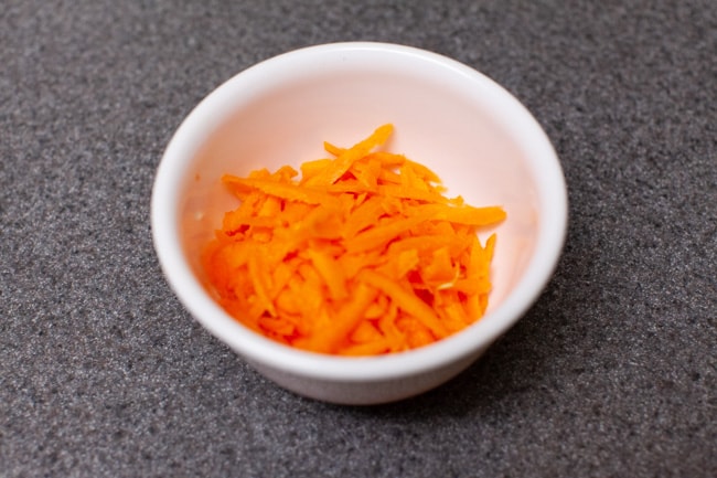 Small white bowl full of shredded carrots on gray countertop for Vegetarian Dumplings from thelittlekitchen.net
