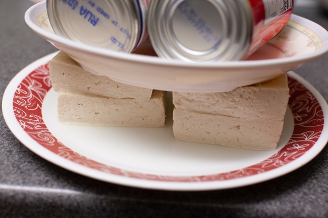 4 slabs of tofu on a plate being pressed to release liquid  from thelittlekitchen.net