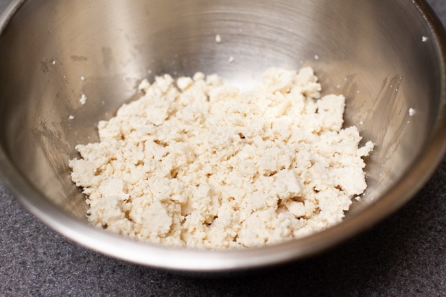 Metal mixing bowl filled with crumbled tofu for dumplings