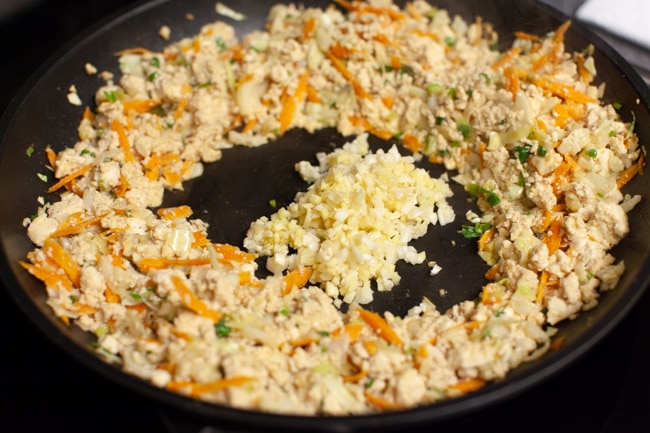 Vegetarian Dumpling filling pushed to sides of skillet with minced garlic and ginger in the middle