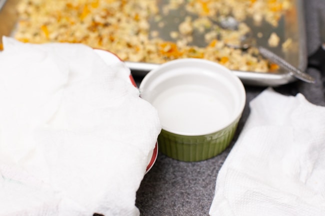 Damp towels over dumpling wrappers to keep them moist with small bowl of water and dumpling filling in background from thelittlekitchen.net