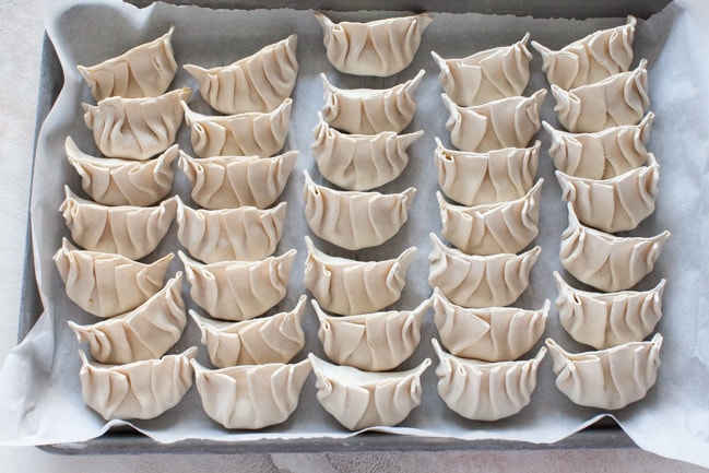 Parchment-lined baking sheet with uncooked Vegetarian Dumplings lined up from thelittlekitchen.net