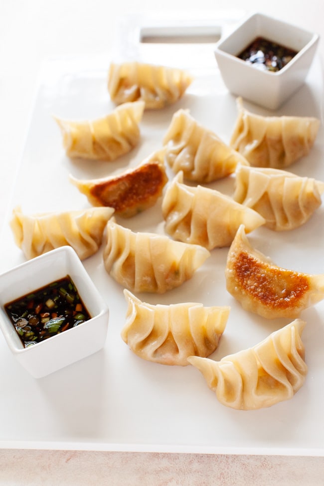 Vegetarian Dumplings on white serving board with two square cups filled with dipping sauce from thelittlekitchen.net
