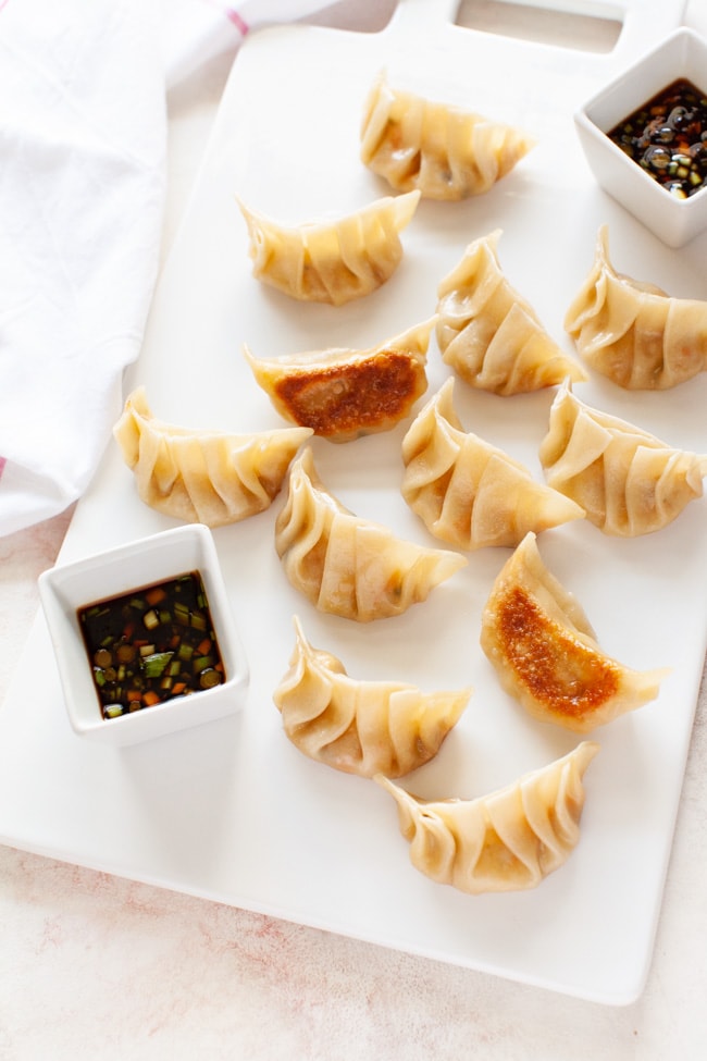 Vegetarian Dumplings on a white serving board with two square cups filled with dipping sauce from thelittlekitchen.net