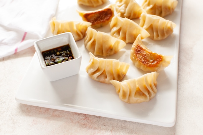 Vegan Dumplings on white serving tray with square dipping sauce bowl and kitchen towel in background from thelittlekitchen.net