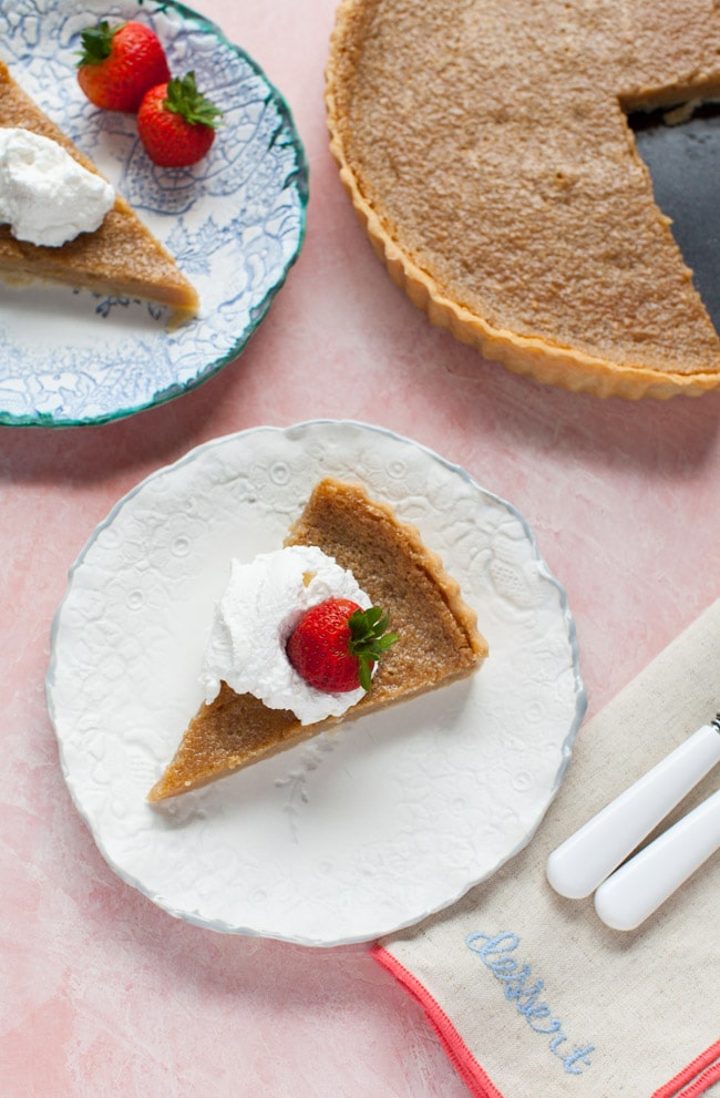 Slice of Sugar Pie on a white plate, topped with whipped cream and strawberry