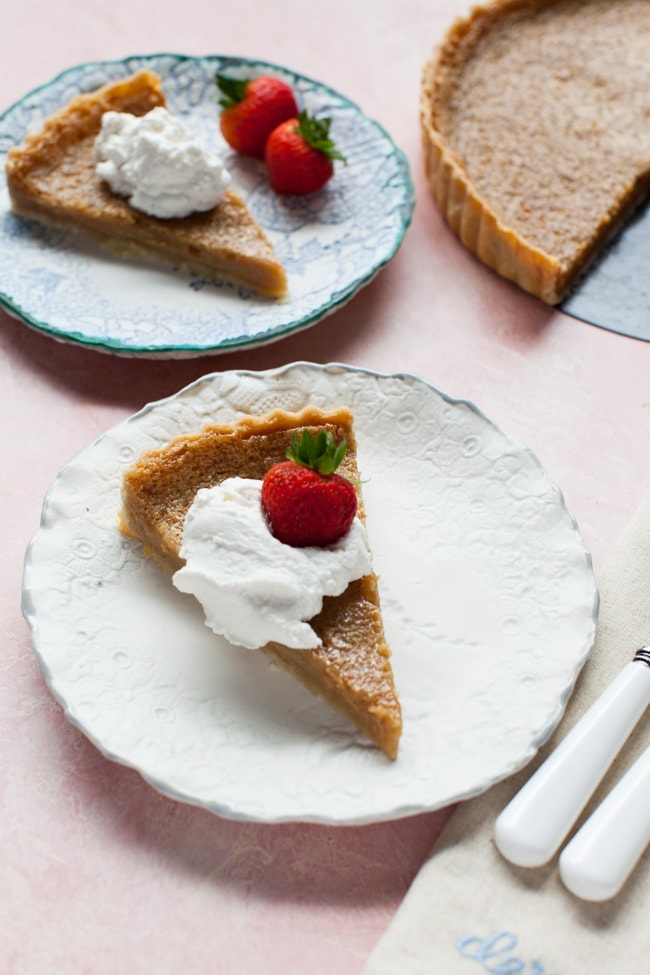 Slice of Sugar Pie on a white plate, topped with whipped cream and strawberry