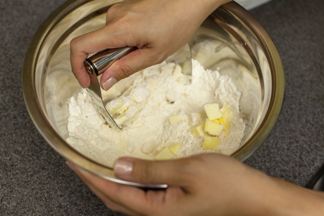 Hands using a pastry blender to cut butter into flour mixture for pie crust