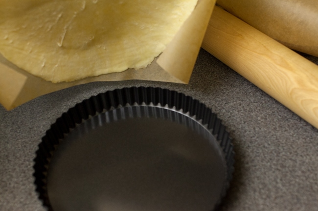 Black tart pan with parchment paper and rolling pin in background