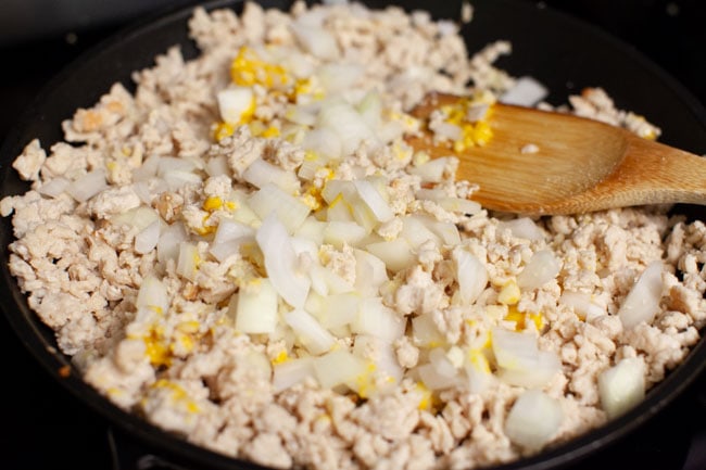 Skillet with cheeseburger egg roll filling cooking and chopped onions on top