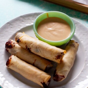 cheeseburger egg rolls on white plate with sauce, egg rolls on a tray in background