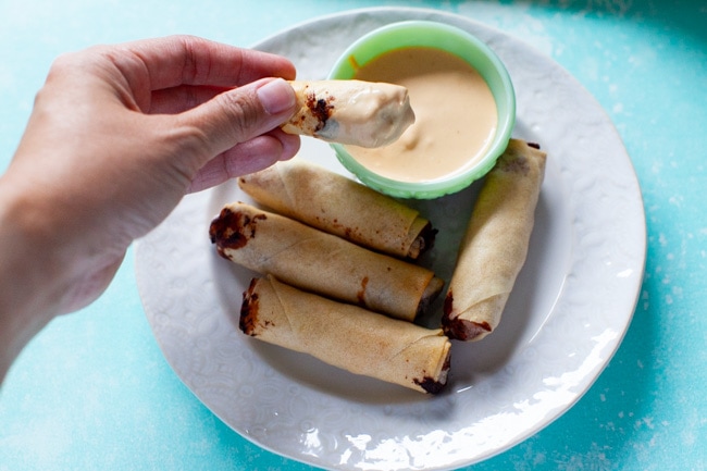 hand holding cheeseburger egg roll just dipped in sauce