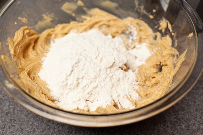 Flour being added to the peanut butter blossom cooking dough in a glass bowl. 