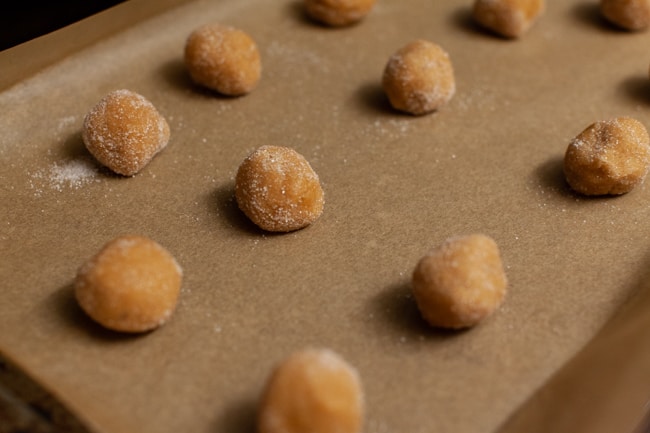 Peanut Butter Blossom Cookie dough balls on a parchment paper lined baking sheet. 