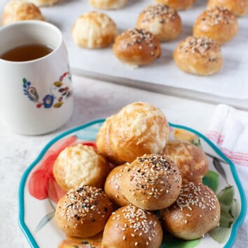 stuffed bagel bites on a floral plate with a cup of tea in the background along with more stuffed bagel bites