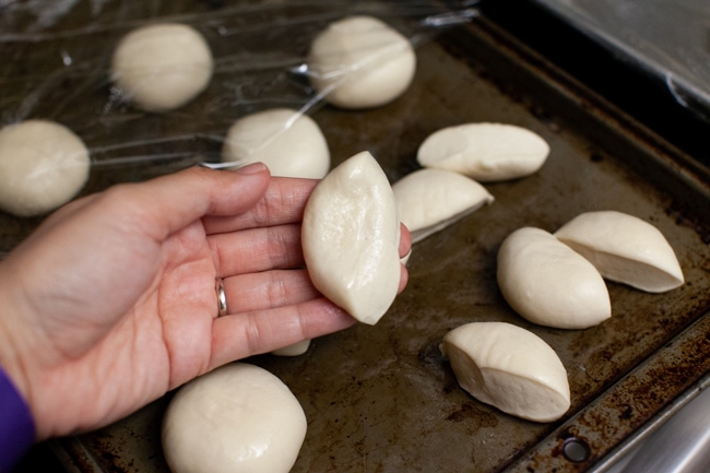 one Rhodes dinner rolls cut in half on a hand with other rolls on a baking sheet in the background