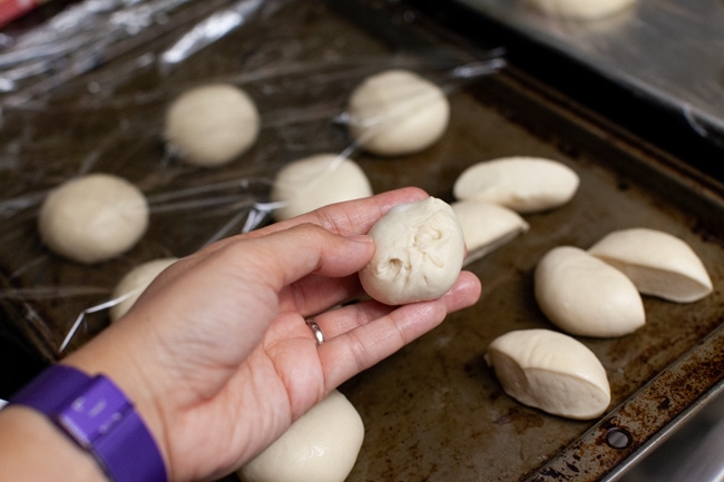 a stuffed bagel bite on a hand with other rolls on a baking sheet in the background