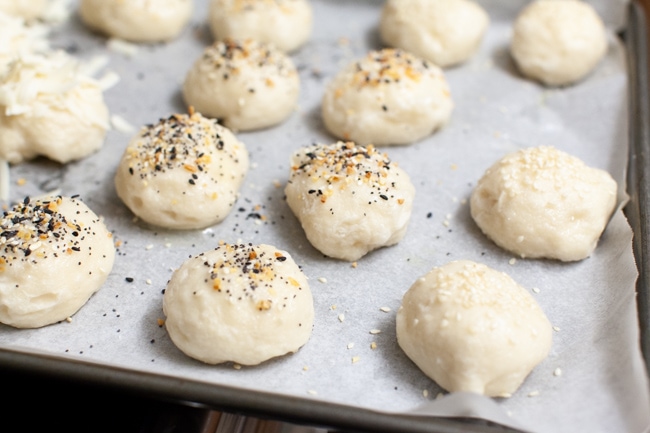 stuffed bagel bites with toppings (sesame seed, everything bagel seasoning) on a parchment paper lined baking sheet