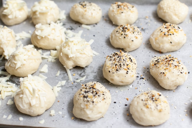 stuffed bagel bites with toppings (shredded asiago , everything bagel seasoning) on a parchment paper lined baking sheet