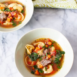 two bowls of beef tortellini soup with a green napkin and two spoons in the background