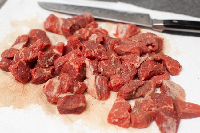 Chopped beef stew meat on paper towels with a knife in the background. 