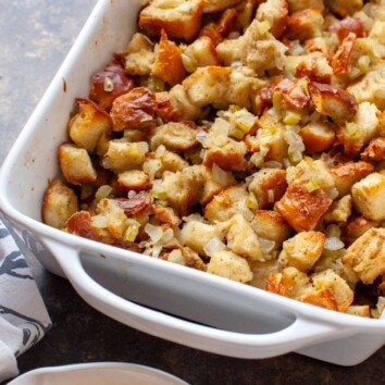 Cooked stuffing recipe in a white baking dish with a bowl of gravy in the foreground